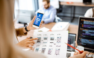 Developers or web designers developing mobile application for banking in the office, close-up on phone and paper sketches